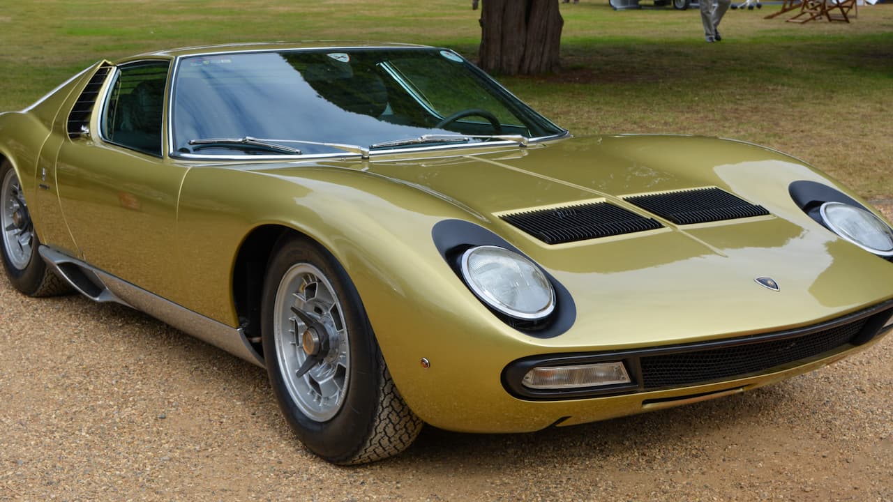 Golden yellow vintage Lamborghini Miura sports car with round headlights parked on grass at outdoor classic car event