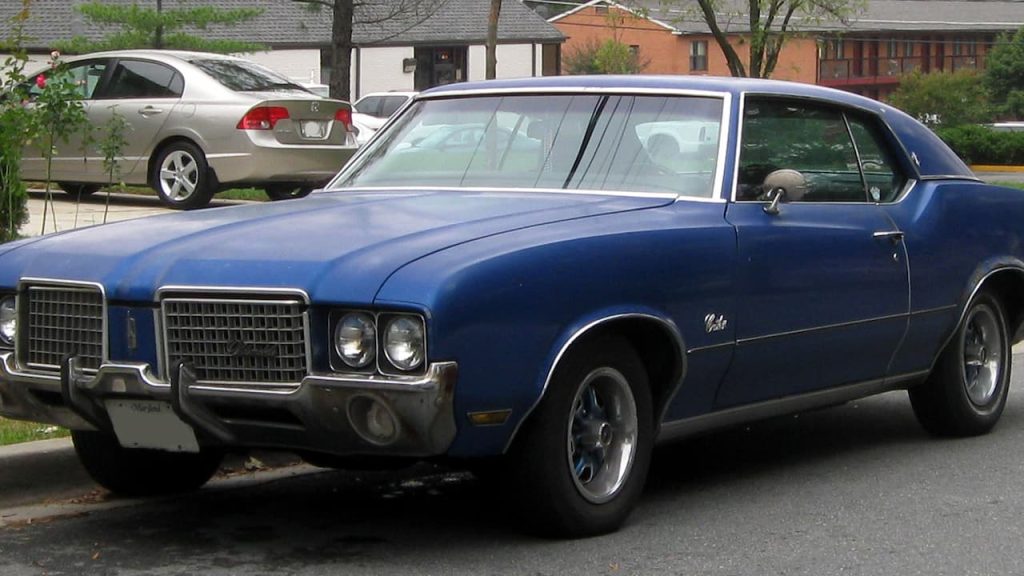 Blue vintage 1972 Oldsmobile Cutlass muscle car with chrome grille and custom wheels parked on residential street