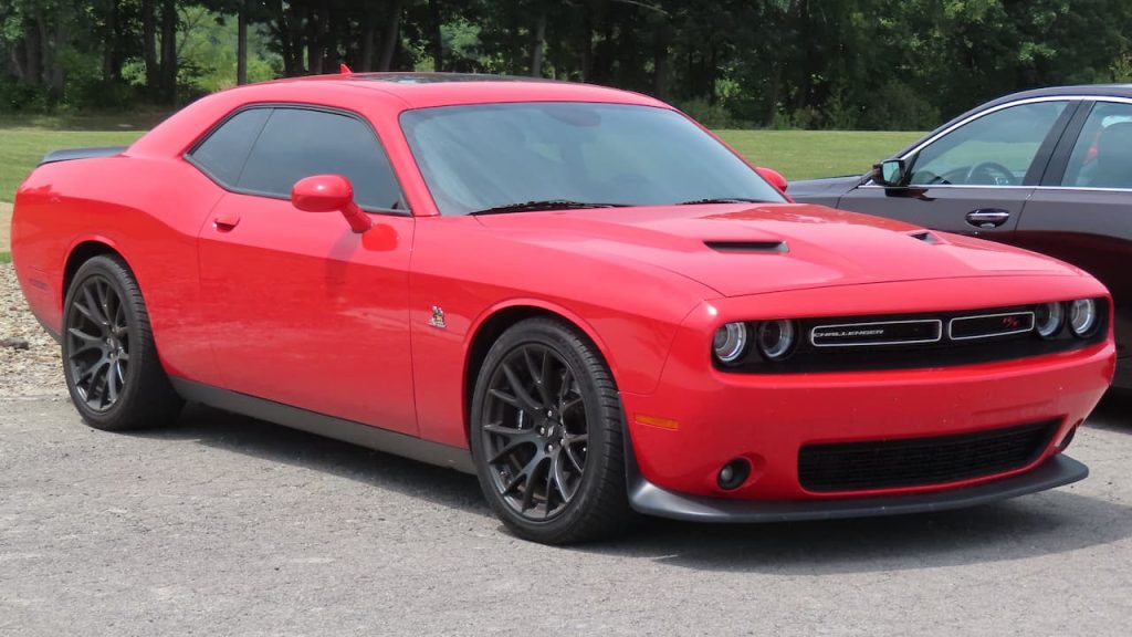 Red 2024 Dodge Challenger R/T muscle car parked on gravel surface with trees in background
