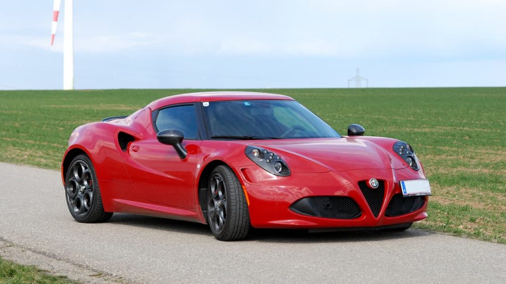  Red Alfa Romeo 4C sports car parked on rural road with green fields and blue sky in background