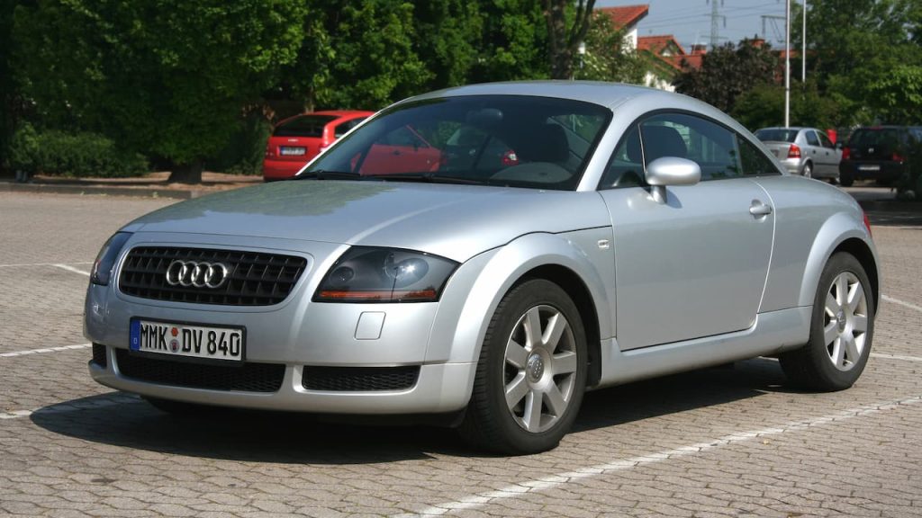 Silver Audi TT with German license plate MWK-DV 840 parked on cobblestone surface surrounded by trees and vehicles