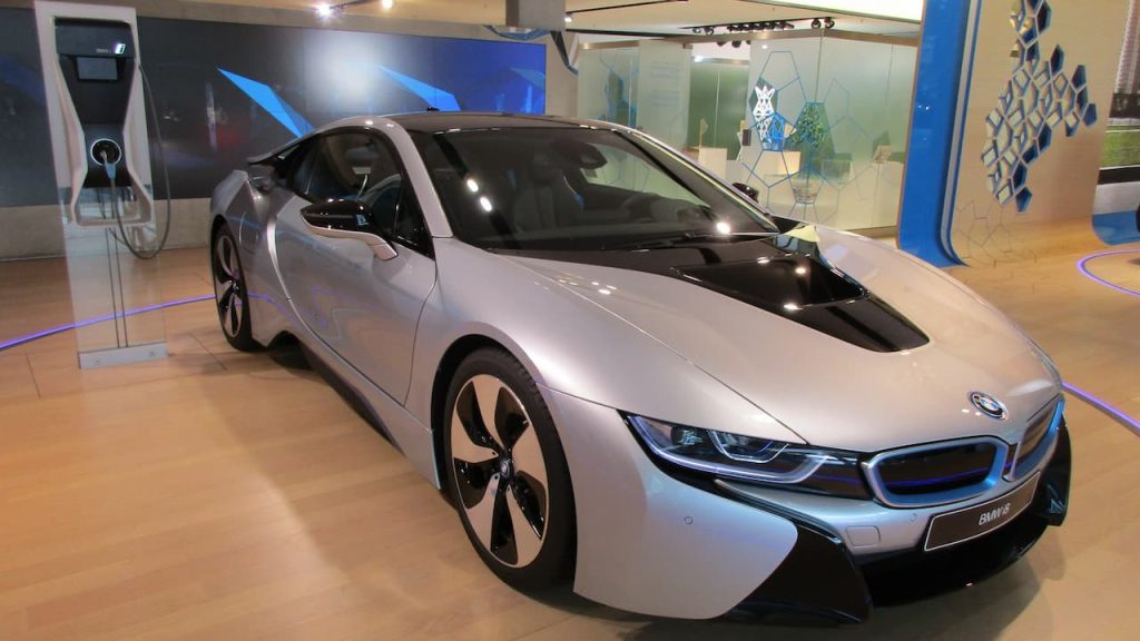 Silver BMW i8 hybrid sports car with black roof displayed in modern showroom with charging station and blue lighting