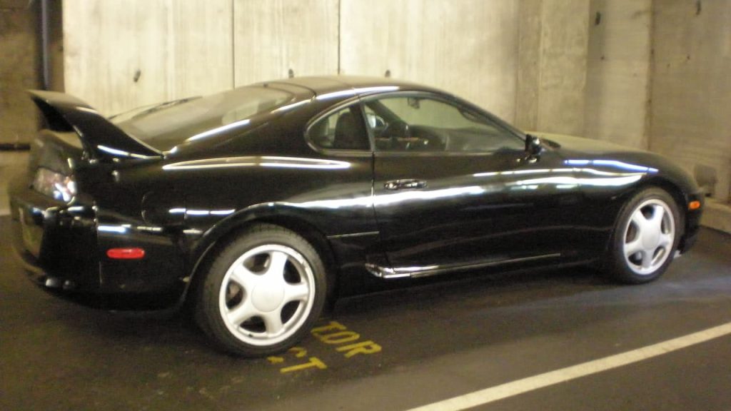 Black Toyota Supra Mark IV with white wheels parked in concrete underground garage with yellow parking markings