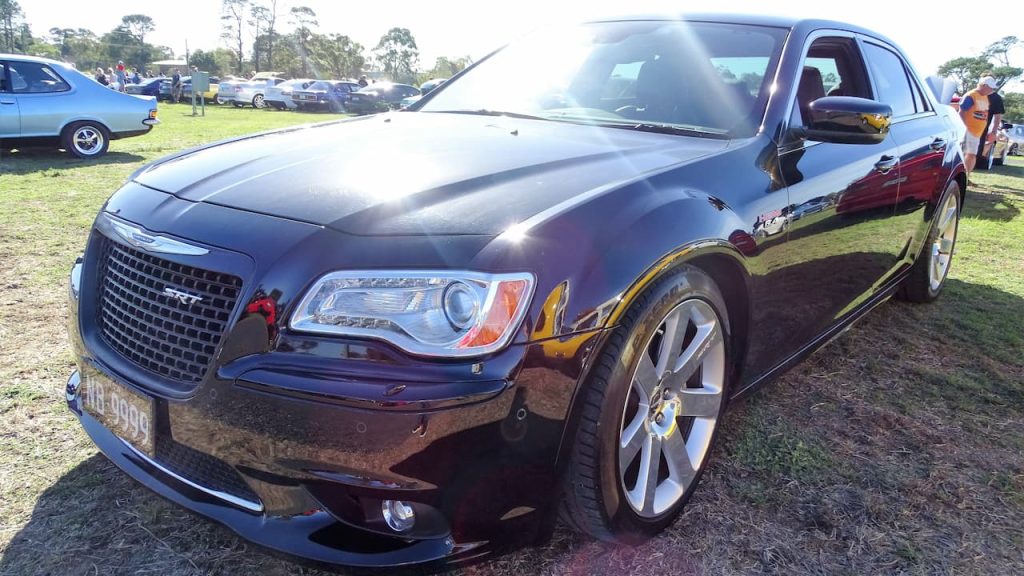 Dark burgundy 2023 Chrysler 300 SRT with chrome grille and large wheels displayed at outdoor car show event