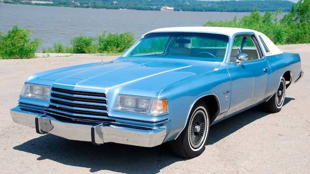 Light blue Dodge Magnum classic muscle car with white vinyl roof parked near waterfront with trees in background