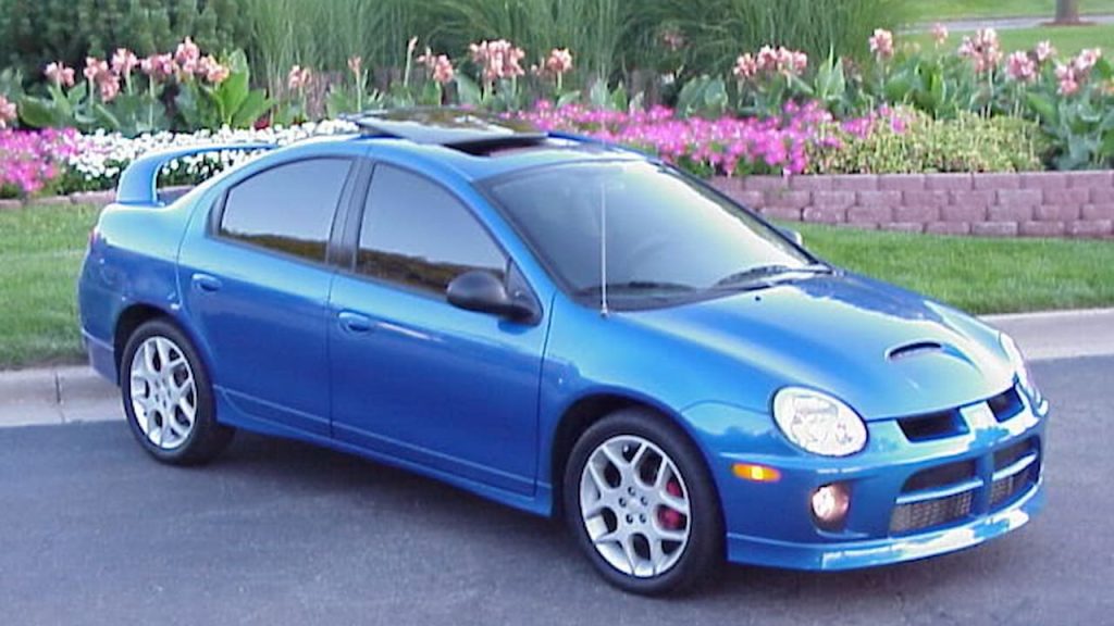 Blue Dodge Neon SRT-4 Factory Hot Rod parked on street with hood scoop, white wheels, and sunroof against colorful flower garden