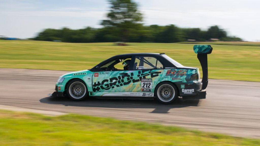 Turquoise Mitsubishi Evo IX RS race car with large rear wing and sponsor decals speeding on racing circuit