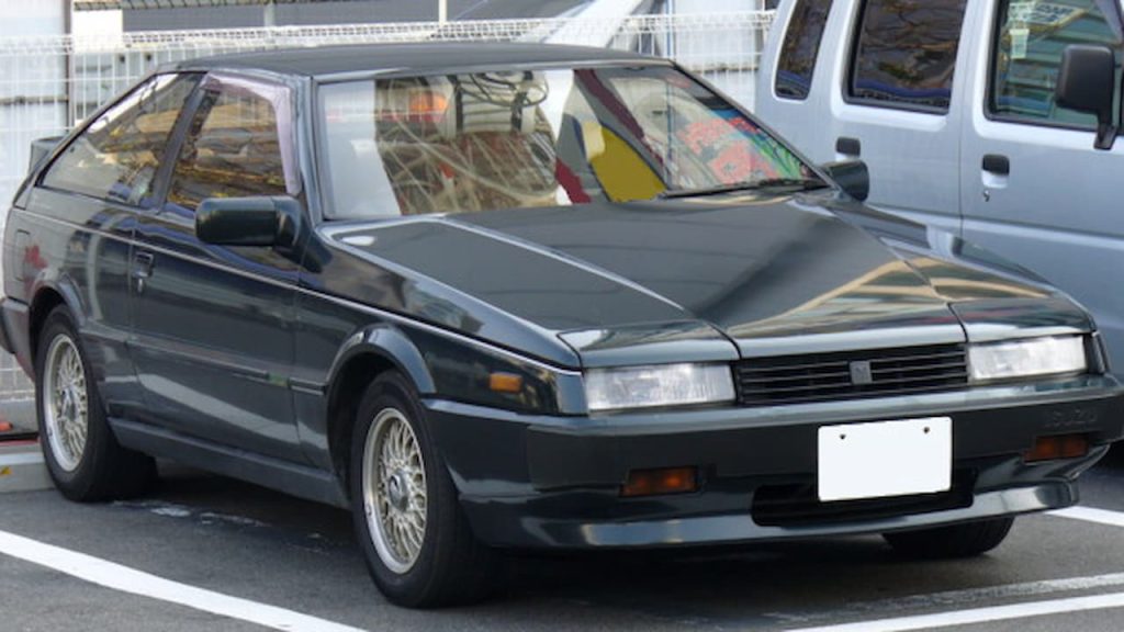 Dark blue Isuzu Piazza with wire wheels parked in lot next to white pickup truck