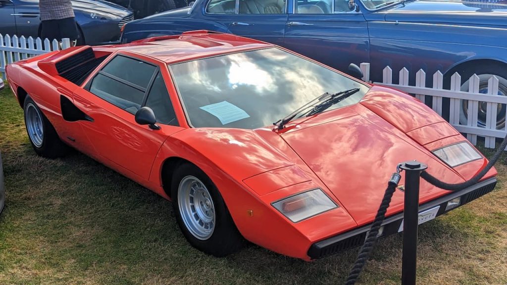 Red Lamborghini Countach with distinctive wedge-shaped design and rear louvers displayed on grass at classic car event