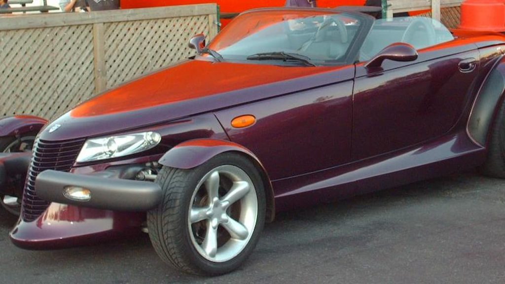 Burgundy Plymouth Prowler convertible sports car with retro hot rod styling parked on street near wooden fence