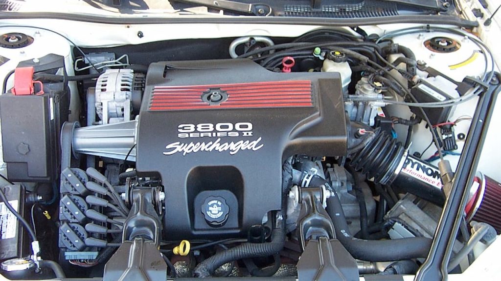  3800 Series II Supercharged V6 engine bay showing black engine cover with red striping, alternator, and various automotive components
