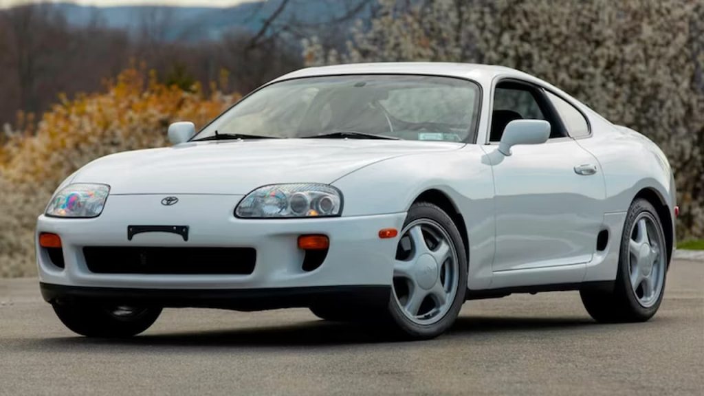 White Toyota Supra MK4 sports car with five-spoke wheels parked on asphalt with autumn foliage background