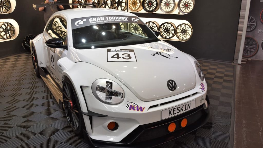 White Volkswagen Beetle race car with number 43 and Gran Turismo branding displayed at automotive show with wheel backdrop