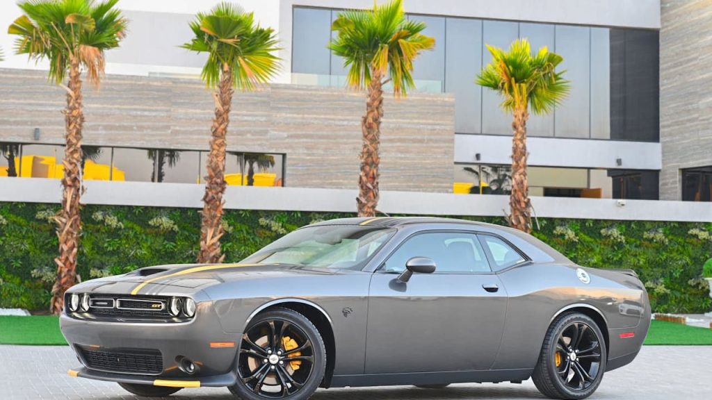Gray 2023 Last Call Dodge Challenger with yellow racing stripes and black wheels parked outside modern building with palm trees