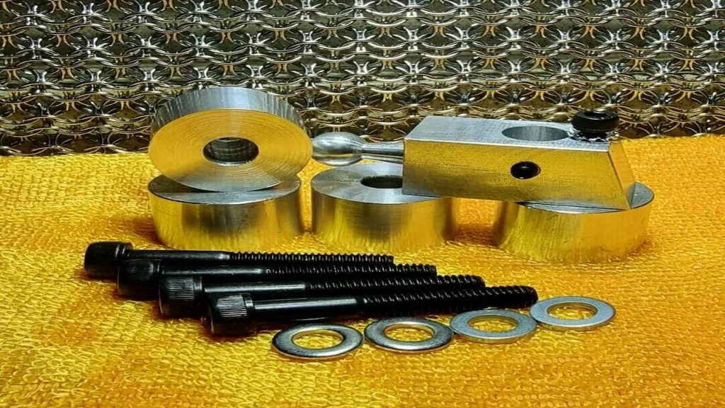 Short-shift kit components including golden cylinder head, pistons, black threaded bolts, and metal washers arranged on yellow surface