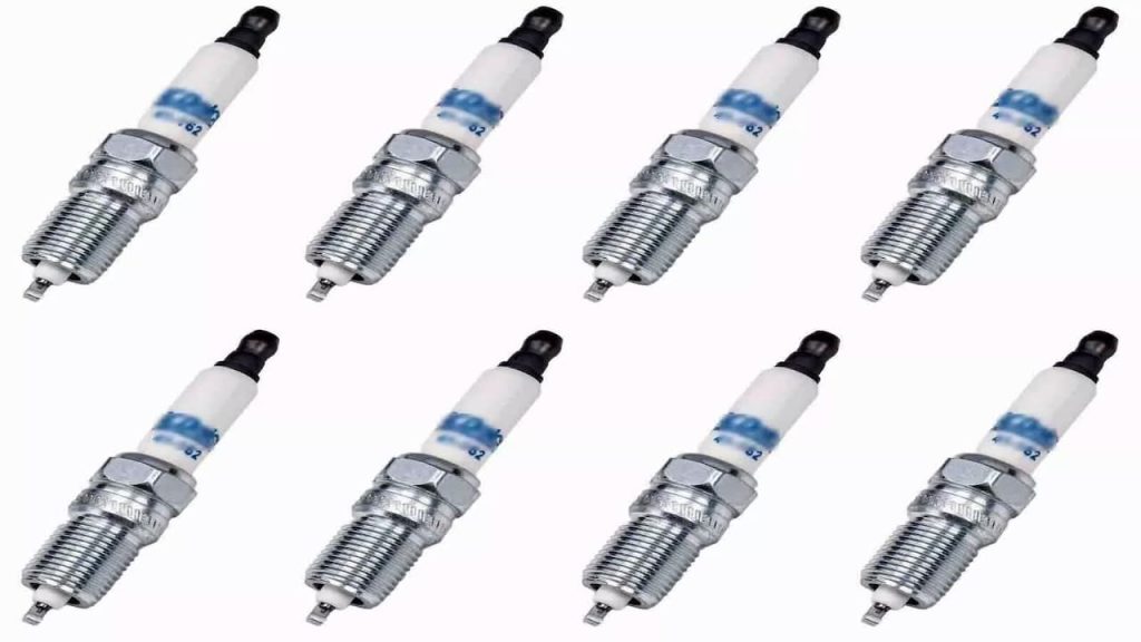 
Eight identical spark plugs arranged in two rows, featuring white ceramic insulators, chrome threading, and black rubber boots