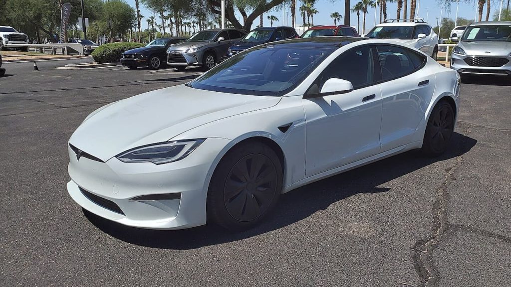 White Tesla Model S Plaid electric sedan with black wheels parked in lot with palm trees and other cars
