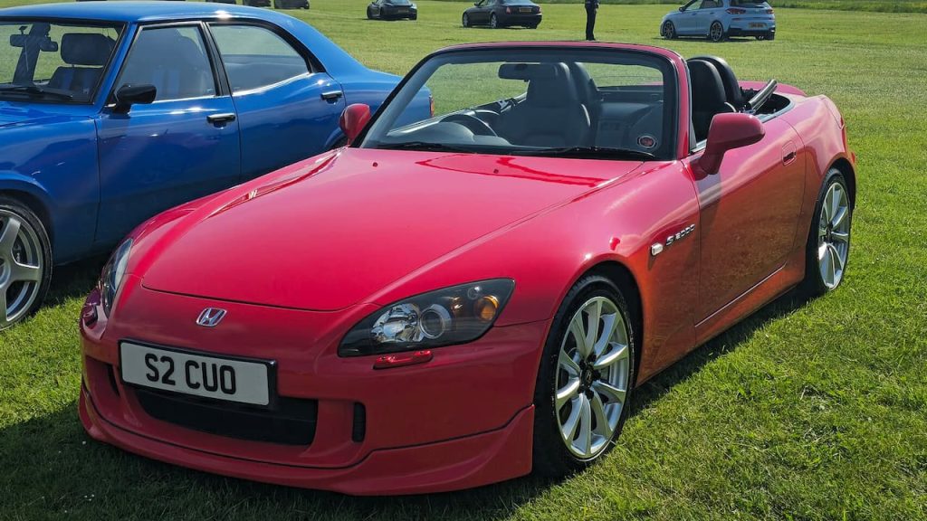 Red Honda S2000 convertible sports car with black soft top and alloy wheels at outdoor car show