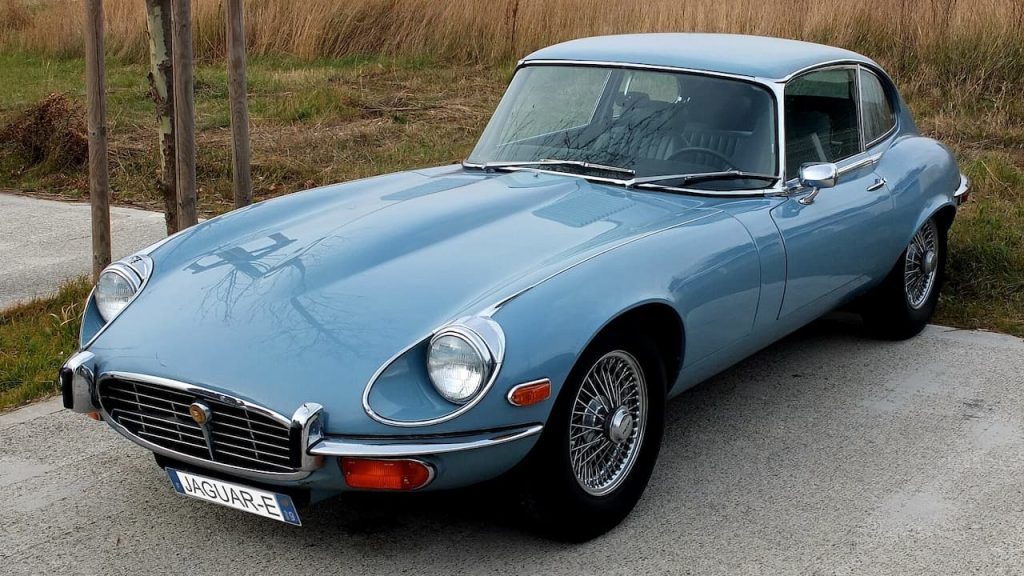 Light blue Jaguar E-Type classic sports car with wire wheels and distinctive long hood parked on pavement