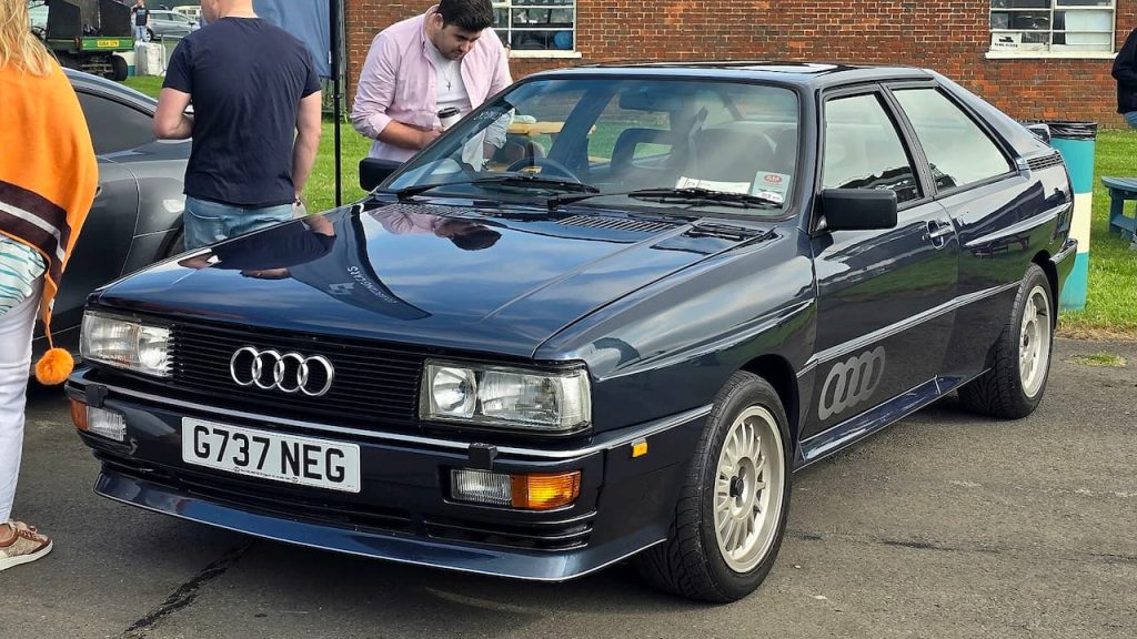 Audi Quattro rally-inspired coupe with distinctive rectangular headlights and white alloy wheels at car show
