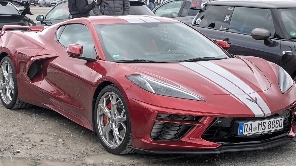 Red Chevrolet Corvette C8 sports car parked at outdoor gathering with silver wheels and white racing stripes