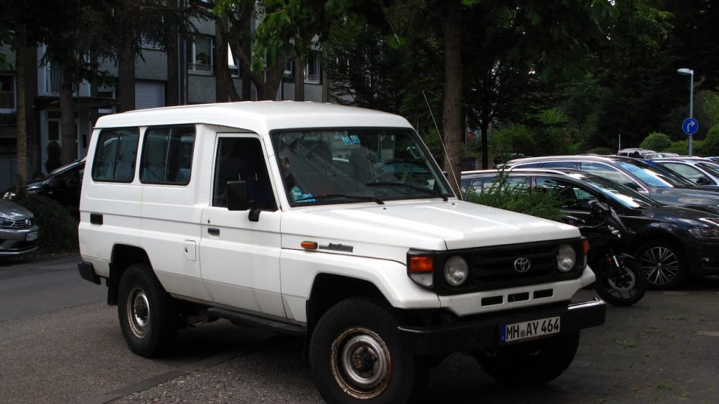 White Toyota Land Cruiser 70 Series SUV with boxy design and round headlights parked in urban area